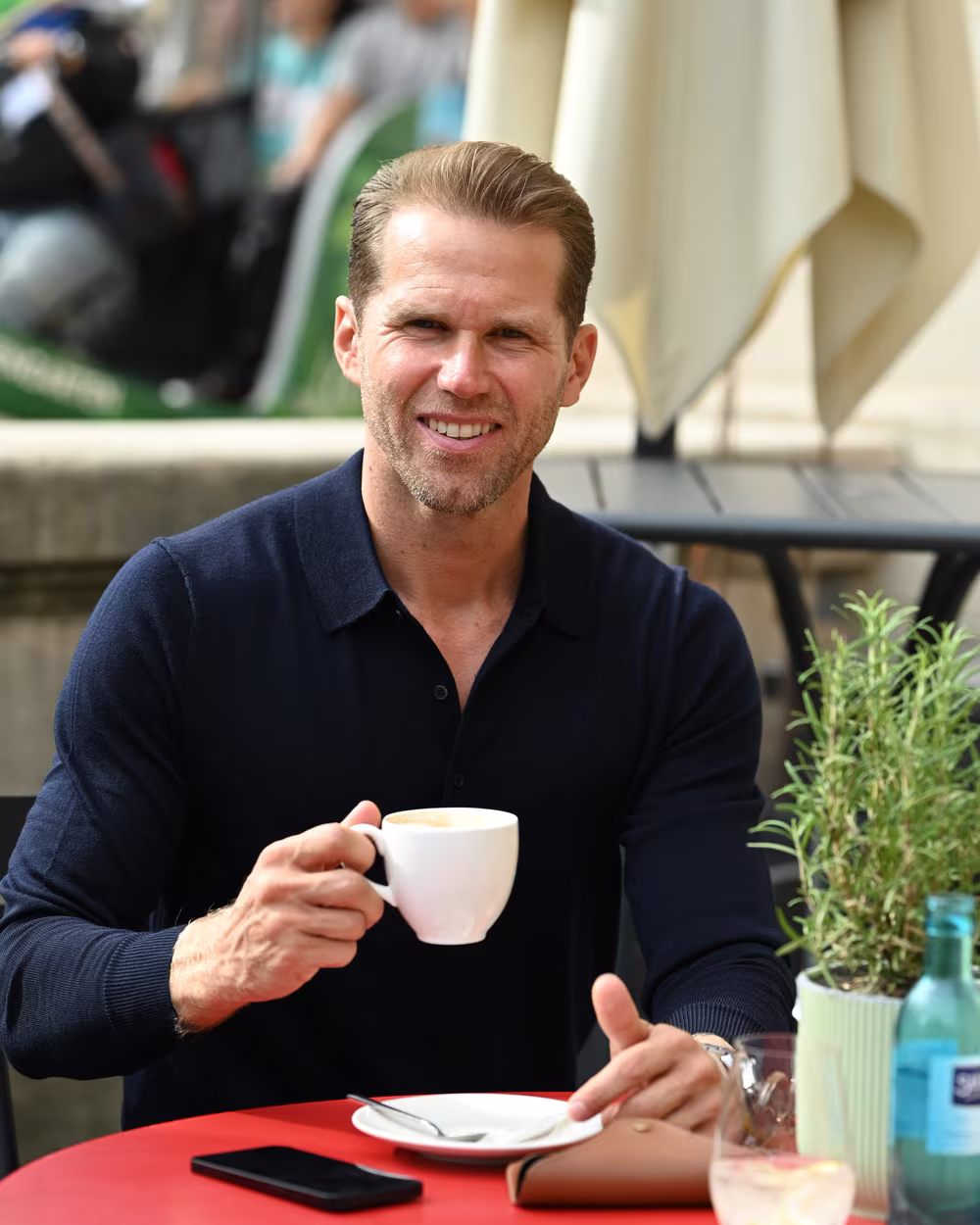 Norman Bartsch mit einer Tasse Kaffee an einem Tisch im Freien.