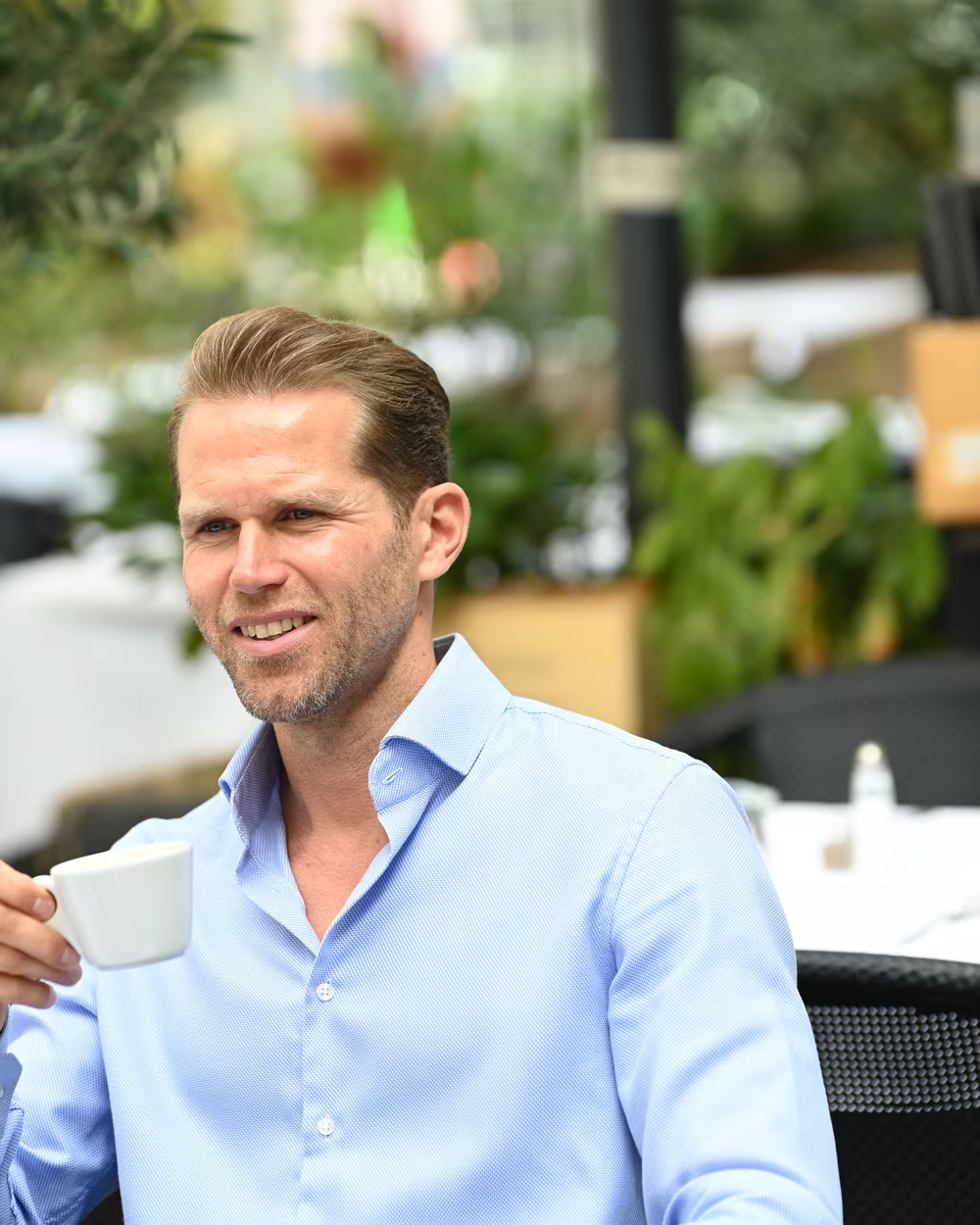 Norman Bartsch im hellblauen Hemd mit einer Tasse in der Hand, im Gespräch.