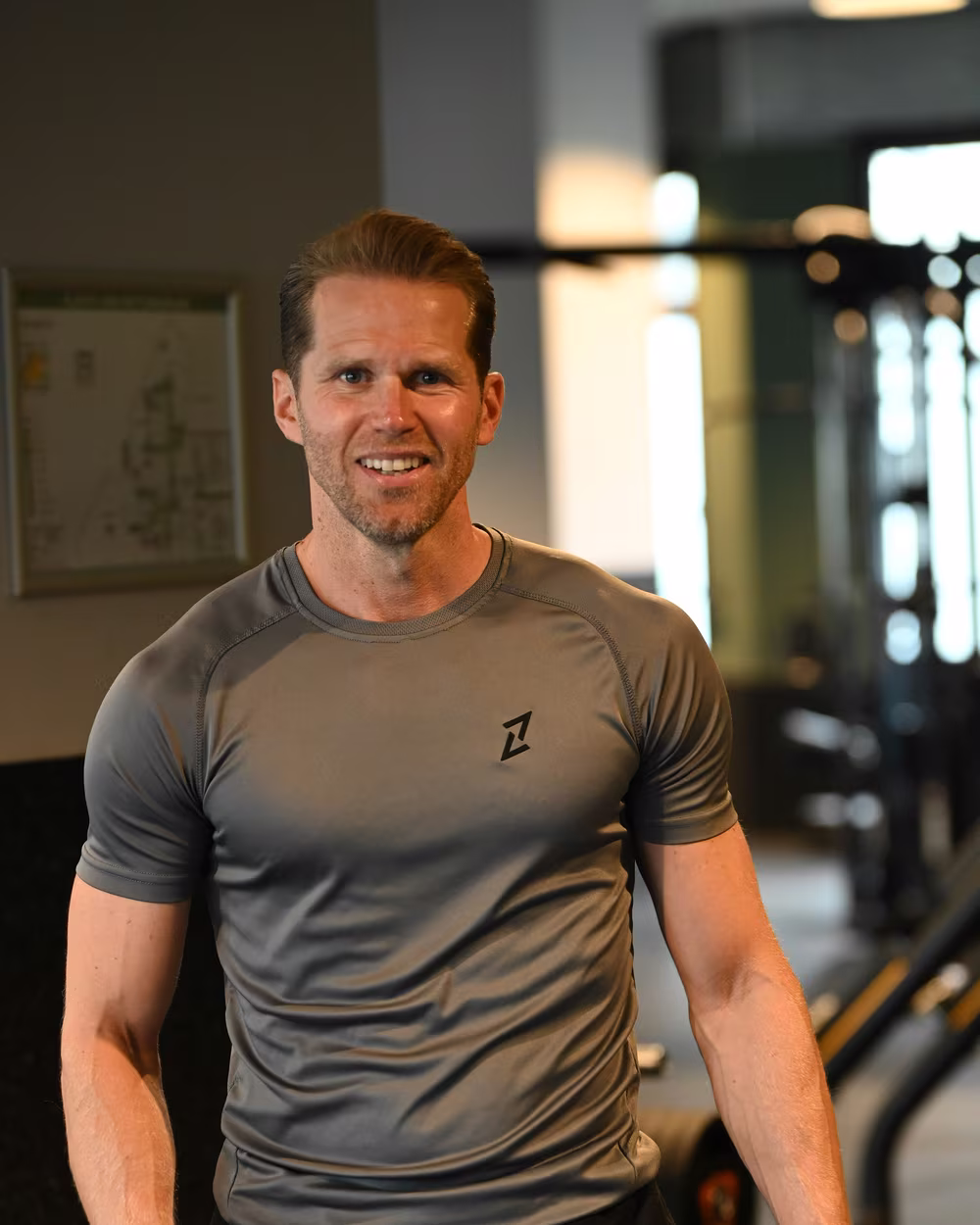 Norman Bartsch im grauen Trainingsshirt im Fitnessstudio.